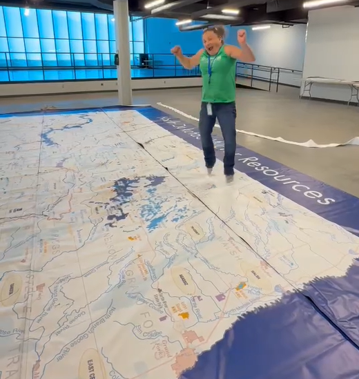 Annie Beck excitedly jumping while standing on 20x30 foot watershed map.