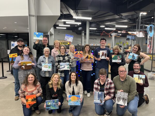 17 adults holding up canvases they painted.