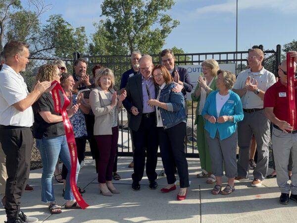 Photo of a group of people, including Beth Demke and Cory Fong, standing in front of the Outdoor Explorium gate after cutting ribbon.