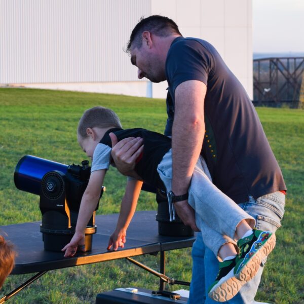Man hold child to look through table top telescope.